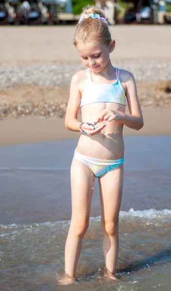 Deniz kıyısında mayo giymiş küçük bir kız oynuyor.