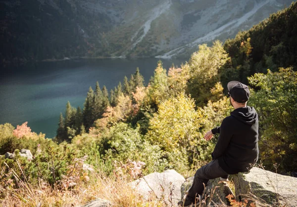 Bir tepenin üstünde dinlenen turist, dağların ve gölün muhteşem manzarasını izliyor..