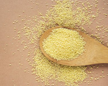 Kahverengi arka planda tahta kaşıkta çiğ kuskus.