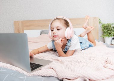 Evdeki kablosuz kulaklıkla dizüstü bilgisayar kullanan mutlu küçük kız..