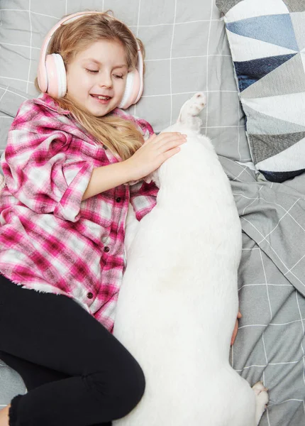 女の子と犬はヘッドフォンでソファに横たわって 彼女のスマートフォンで音楽を聴く — ストック写真