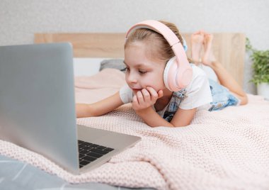 Evdeki kablosuz kulaklıkla dizüstü bilgisayar kullanan mutlu küçük kız..