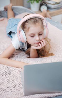 Evdeki kablosuz kulaklıkla dizüstü bilgisayar kullanan mutlu küçük kız..