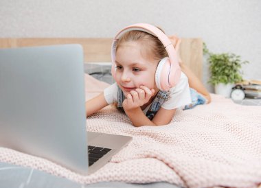 Evdeki kablosuz kulaklıkla dizüstü bilgisayar kullanan mutlu küçük kız..