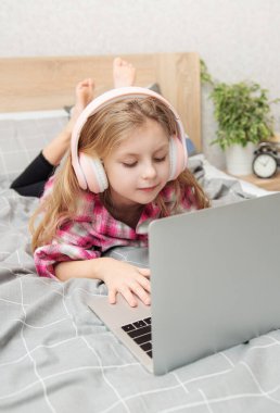 Evdeki kablosuz kulaklıkla dizüstü bilgisayar kullanan mutlu küçük kız..