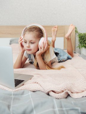 Evdeki kablosuz kulaklıkla dizüstü bilgisayar kullanan mutlu küçük kız..