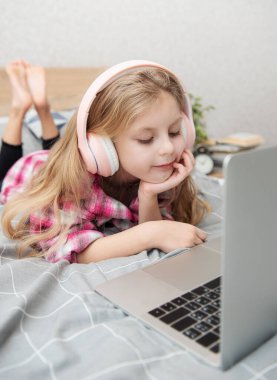 Evdeki kablosuz kulaklıkla dizüstü bilgisayar kullanan mutlu küçük kız..