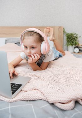 Evdeki kablosuz kulaklıkla dizüstü bilgisayar kullanan mutlu küçük kız..