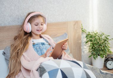 Kulaklık takan tatlı küçük kız evde tablet kullanıyor.