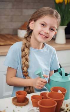 Evdeki masada oturan küçük kız, saksılara tohum ekiyor. Evde bahçe işleri. 