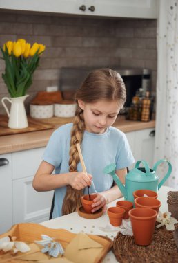 Evdeki masada oturan küçük kız, saksılara tohum ekiyor. Evde bahçe işleri. 