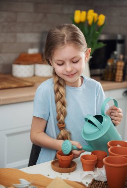 Evdeki masada oturan küçük kız, saksılara tohum ekiyor. Evde bahçe işleri. 