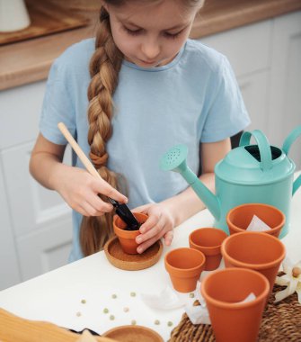 Evdeki masada oturan küçük kız, saksılara tohum ekiyor. Evde bahçe işleri. 