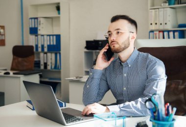 Ofiste dizüstü bilgisayarıyla çalışan gömlekli genç bir iş adamı.