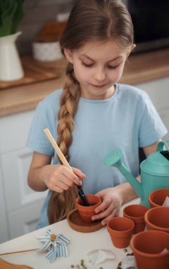 Evdeki masada oturan küçük kız, saksılara tohum ekiyor. Evde bahçe işleri. 
