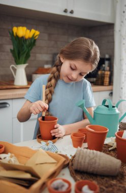Evdeki masada oturan küçük kız, saksılara tohum ekiyor. Evde bahçe işleri. 