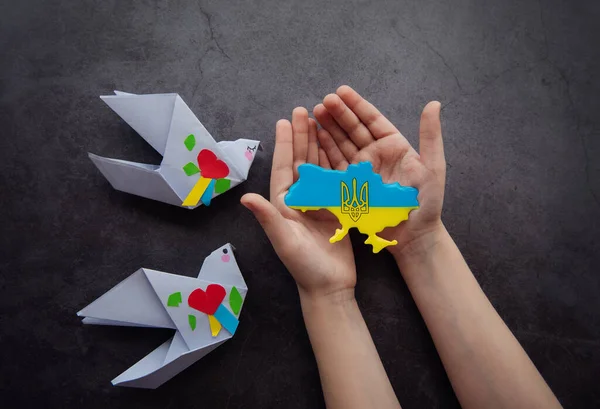 Hands holding the shape of Ukraine border with color flag and paper birds. Stand with Ukraine.
