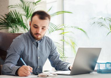 Ofiste dizüstü bilgisayarıyla çalışan gömlekli genç bir iş adamı.