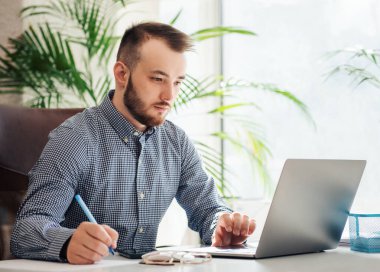 Ofiste dizüstü bilgisayarıyla çalışan gömlekli genç bir iş adamı.