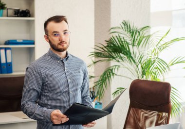 Ofiste dizüstü bilgisayarıyla çalışan gömlekli genç bir iş adamı.