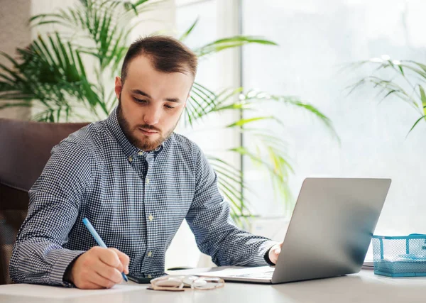 Ofiste dizüstü bilgisayarıyla çalışan gömlekli genç bir iş adamı.