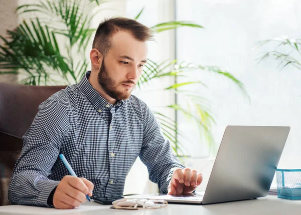 Ofiste dizüstü bilgisayarıyla çalışan gömlekli genç bir iş adamı.