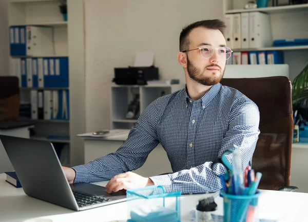 Ofiste dizüstü bilgisayarıyla çalışan gömlekli genç bir iş adamı.
