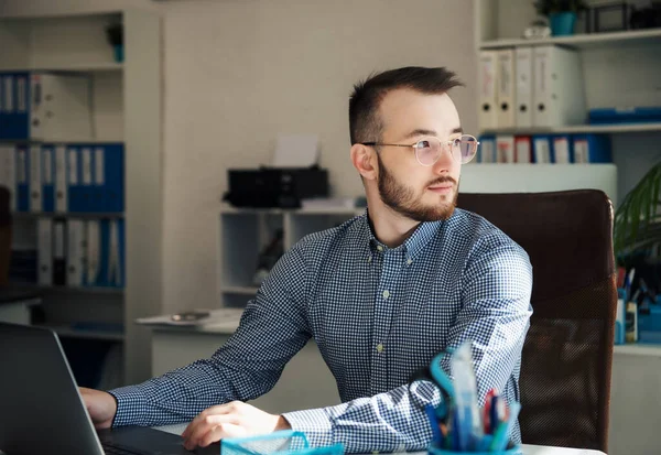 Ofiste dizüstü bilgisayarıyla çalışan gömlekli genç bir iş adamı.