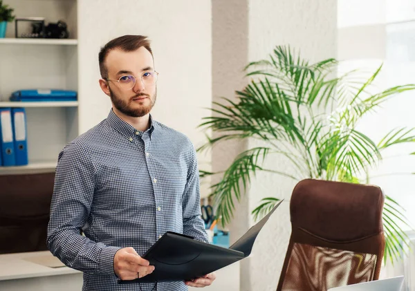 Ofiste dizüstü bilgisayarıyla çalışan gömlekli genç bir iş adamı.