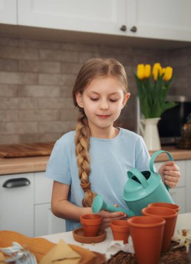 Evdeki masada oturan küçük kız, saksılara tohum ekiyor. Evde bahçe işleri. 
