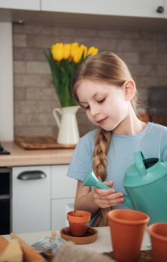 Evdeki masada oturan küçük kız, saksılara tohum ekiyor. Evde bahçe işleri. 