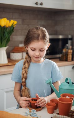 Evdeki masada oturan küçük kız, saksılara tohum ekiyor. Evde bahçe işleri. 