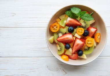 Tahta arka planda bir kasede sağlıklı taze meyve salatası.