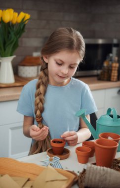 Evdeki masada oturan küçük kız, saksılara tohum ekiyor. Evde bahçe işleri. 