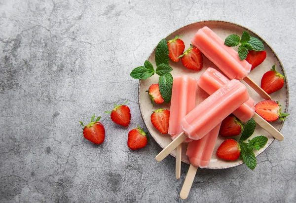 Homemade frozen strawberry ice cream popsicles and fresh strawberries on a concrete background. Summer dessert