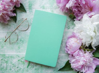 Düz kağıt defter, gözlükler, yeşil ahşap arka planda şakayık çiçekleri.