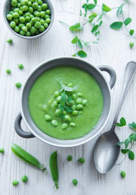 Fresh green pea soup bowl on white wooden background