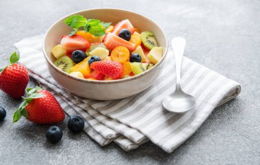Beton arka planda bir kasede sağlıklı taze meyve salatası.