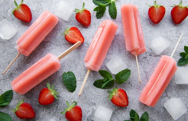 Homemade frozen strawberry ice cream popsicles, ice cubes and fresh strawberries on a concrete background. Summer dessert