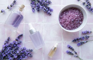 Spa products and lavender flowers on a pink tile background.  Aromatherapy lavender bath salt and massage oil