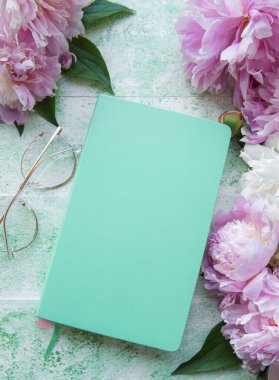 Düz kağıt defter, gözlükler, yeşil ahşap arka planda şakayık çiçekleri.