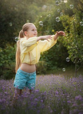 Beautiful little girl catches soap bubbles in a field with lavender 
