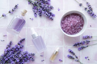 Spa products and lavender flowers on a pink tile background.  Aromatherapy lavender bath salt and massage oil