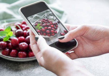 Hands holding a smartphone and taking a  photography of cherries in plate