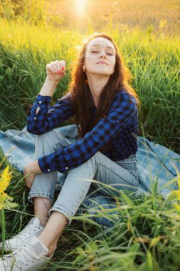 Çayırda genç ve güzel bir kadının portresi. Gün batımını seyrediyor. Yaz akşamının tadını çıkarıyor..