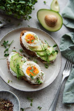 Ekmek tostu, haşlanmış yumurta, avokado dilimi, tabakta mikroyeşiller, kahvaltı zamanı.