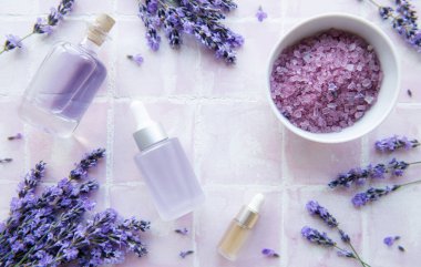 Spa products and lavender flowers on a pink tile background.  Aromatherapy lavender bath salt and massage oil