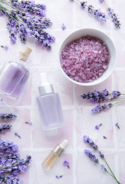 Spa products and lavender flowers on a pink tile background.  Aromatherapy lavender bath salt and massage oil