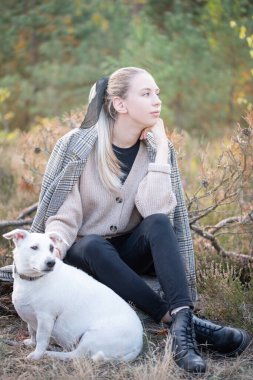 Genç ve çekici bir kadın sonbahar parkında köpekle oynuyor.