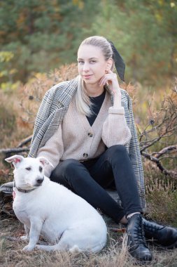Genç ve çekici bir kadın sonbahar parkında köpekle oynuyor.